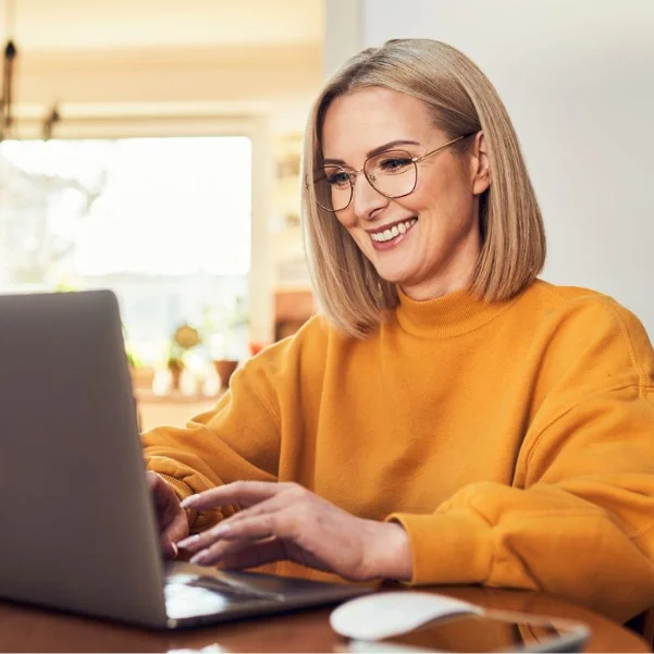 Brevo: Eine Frau im orangen Pulli sitzt vor ihrem Laptop